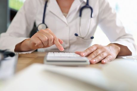 Foto: Ärztin arbeitet auf Taschenrechner im Büro